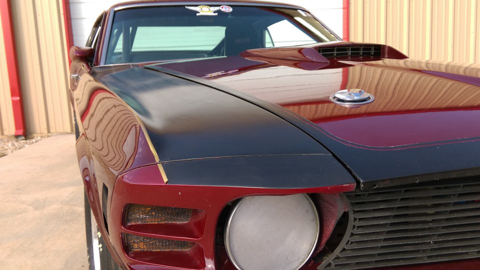 Red fastback muscle car front corner, black hood, missing headlight, blacked-out grille