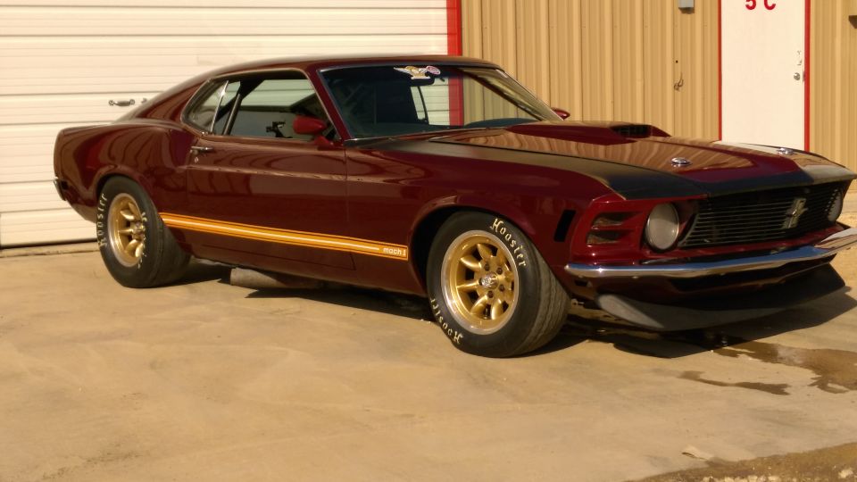 Maroon Mustang Mach 1 fastback outside a shop, gold stripe and gold five-spoke wheels