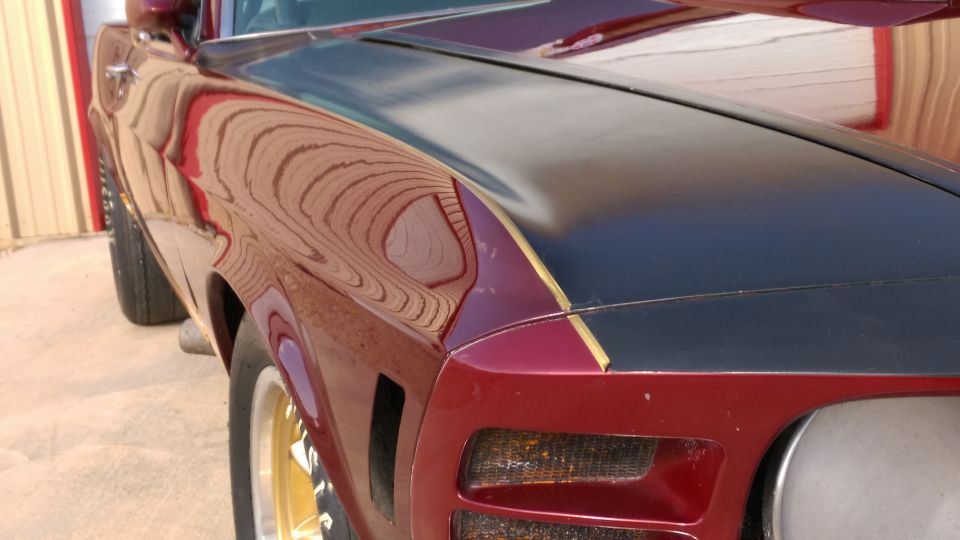 Left front fender of red muscle car with gold-striped black hood and gold wheel