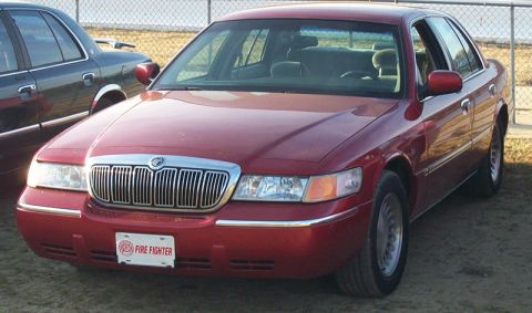 1993 Mercury Grand Marquis - A red sedan is parked next to another vehicle, with a fence in the background.