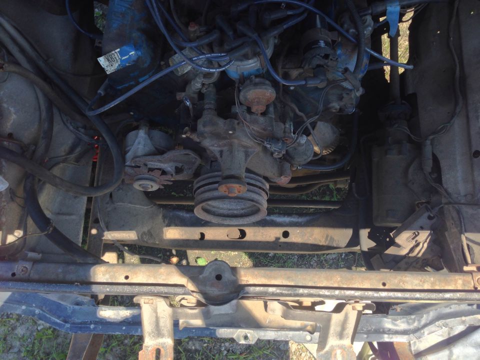 Engine bay with hoses, wires, and engine components visible. Some rust on metal parts