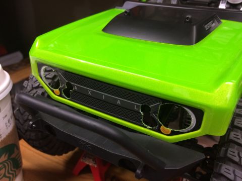 1989 Ford Bronco - Close-up of a bright green RC car's front grille and bumper, with a coffee cup nearby.
