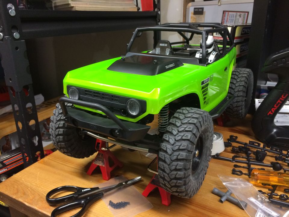 Green RC rock crawler model on jack stands, with tools and parts nearby