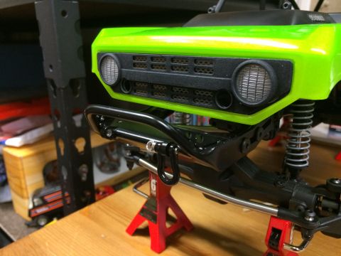 1989 Ford Bronco - Close-up of the front grille and bumper assembly of a bright green radio-controlled vehicle, supported by red jack stands.