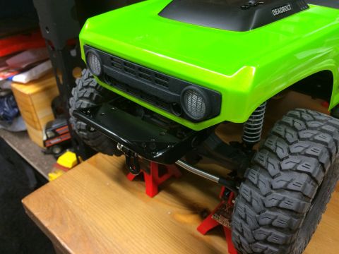 1989 Ford Bronco - A close-up view of a bright green RC car body, a black grille and bumper, supported by red jack stands.