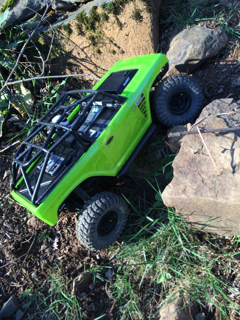 Green RC rock crawler with a roll cage on rocky terrain