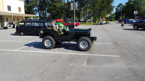 1948 Jeep Wrangler - A dark green Jeep CJ is parked in a lot with other vehicles visible in the background.