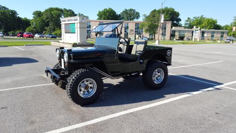 1948 Jeep Wrangler - This 1948 Jeep CJ-3A is parked in a lot, showing its distinctive front 3/4 profile with a folded windshield and military star emblem.