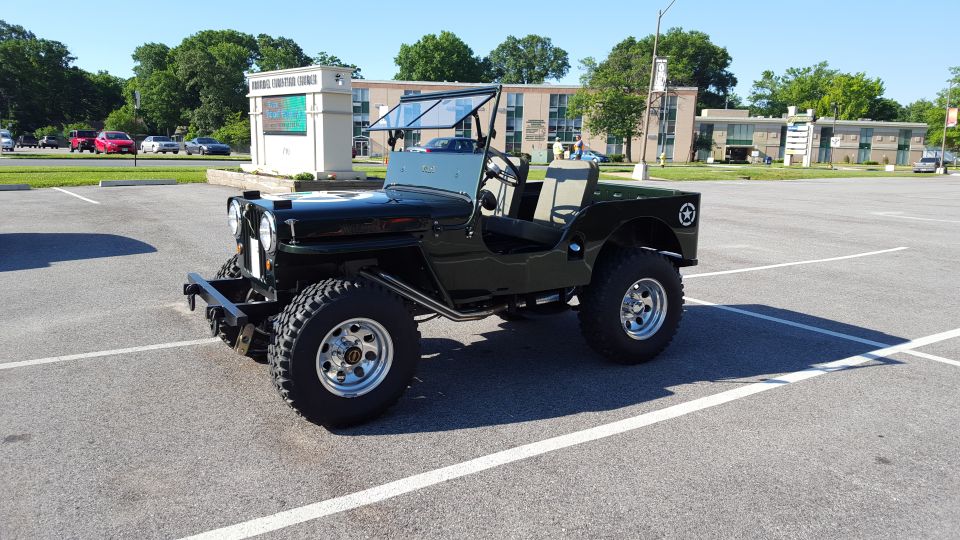 Black Jeep CJ-3A parked in a lot, front 3/4 view. It has a black grille, round headlights, and a folded windshield