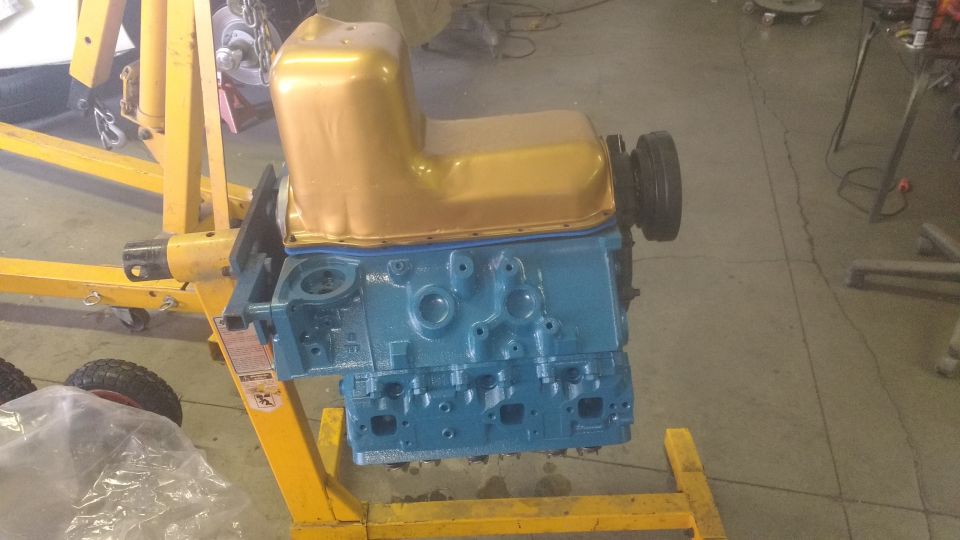 Blue engine block with gold oil pan on yellow engine hoist