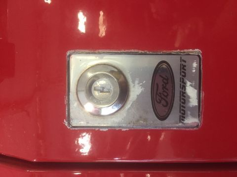 1995 Ford Bronco - Close-up of a Ford Motorsport emblem and lock cylinder on a red vehicle panel.