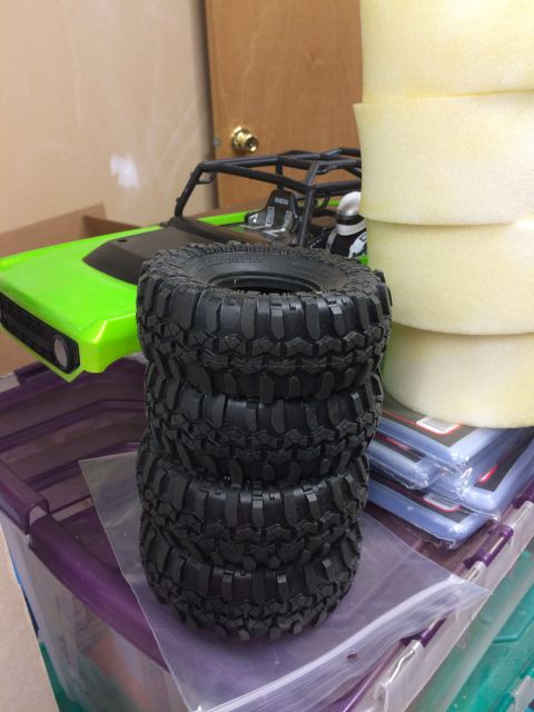 1989 Ford Bronco - Four off-road tires are stacked in front of a green RC car chassis, with foam inserts visible to the right.