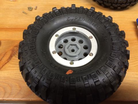 1989 Ford Bronco - A close-up view of a single RC car tire with aggressive tread and a silver and gray wheel.