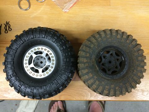 1989 Ford Bronco - A new RC car tire sits next to a muddy, used one on a wooden table.