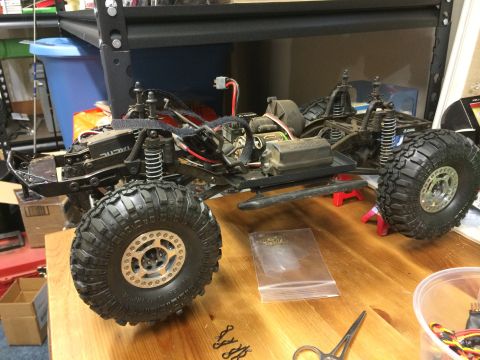 1989 Ford Bronco - A remote-controlled rock crawler chassis sits on a wooden surface, showing its suspension and large off-road tires.