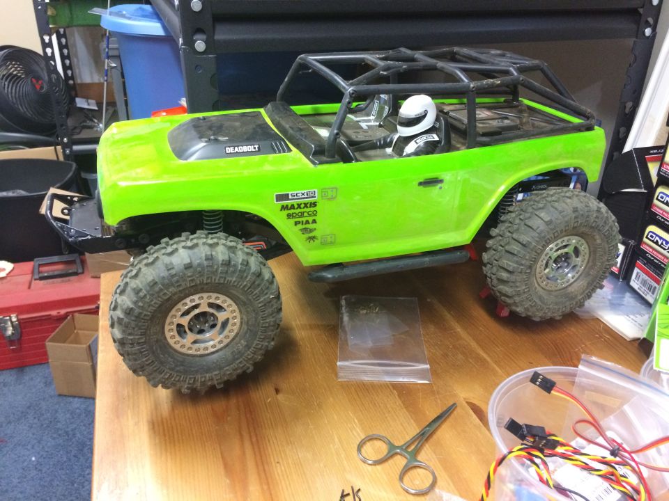 Green RC rock crawler toy truck with roll cage and driver figure. "DEADBOLT" visible on hood