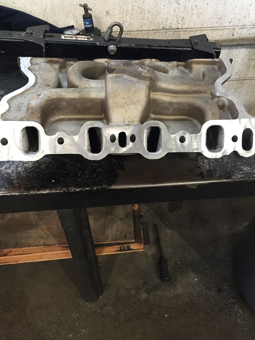 Aluminum intake manifold with six intake ports and four exhaust ports, resting on a workbench
