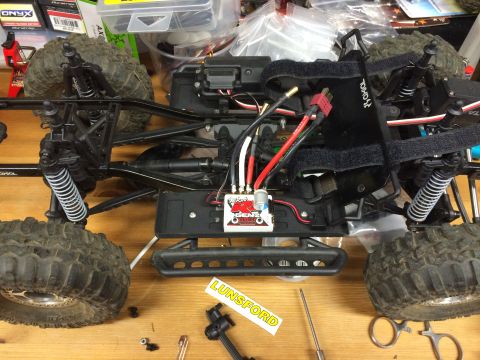 1989 Ford Bronco - The chassis of a remote-controlled rock crawler sits on a wooden surface, surrounded by various electronic components and tools.