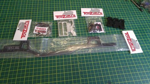 1989 Ford Bronco - Various unassembled parts for an RC car, including chassis rails and suspension components, are displayed on a cutting mat.