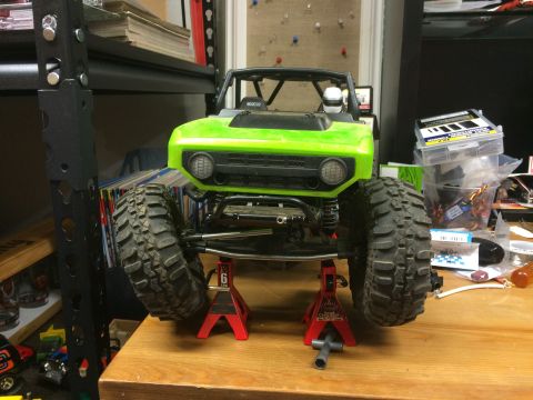1989 Ford Bronco - A green RC car body is elevated on red jack stands, showing its front end and large off-road tires.