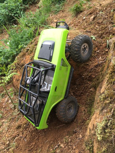 1989 Ford Bronco - An overturned green RC rock crawler is stuck on a steep, muddy incline surrounded by vegetation.