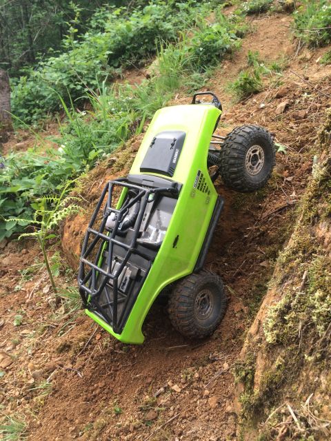 1989 Ford Bronco - This lime green remote control rock crawler is navigating a steep dirt incline with dense foliage in the background.