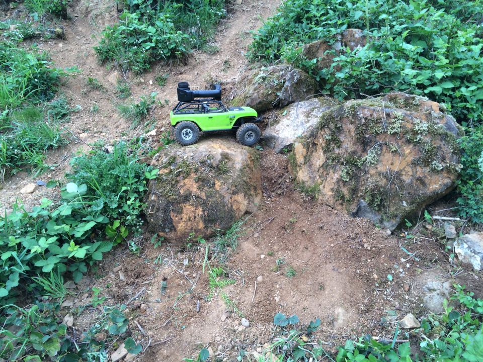 Green remote-control rock crawler with roof rack on a dirt path between rocks