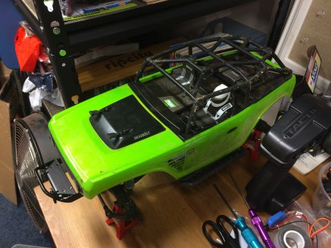 1989 Ford Bronco - RC car body and remote control on a workbench, with tools and a fan nearby.