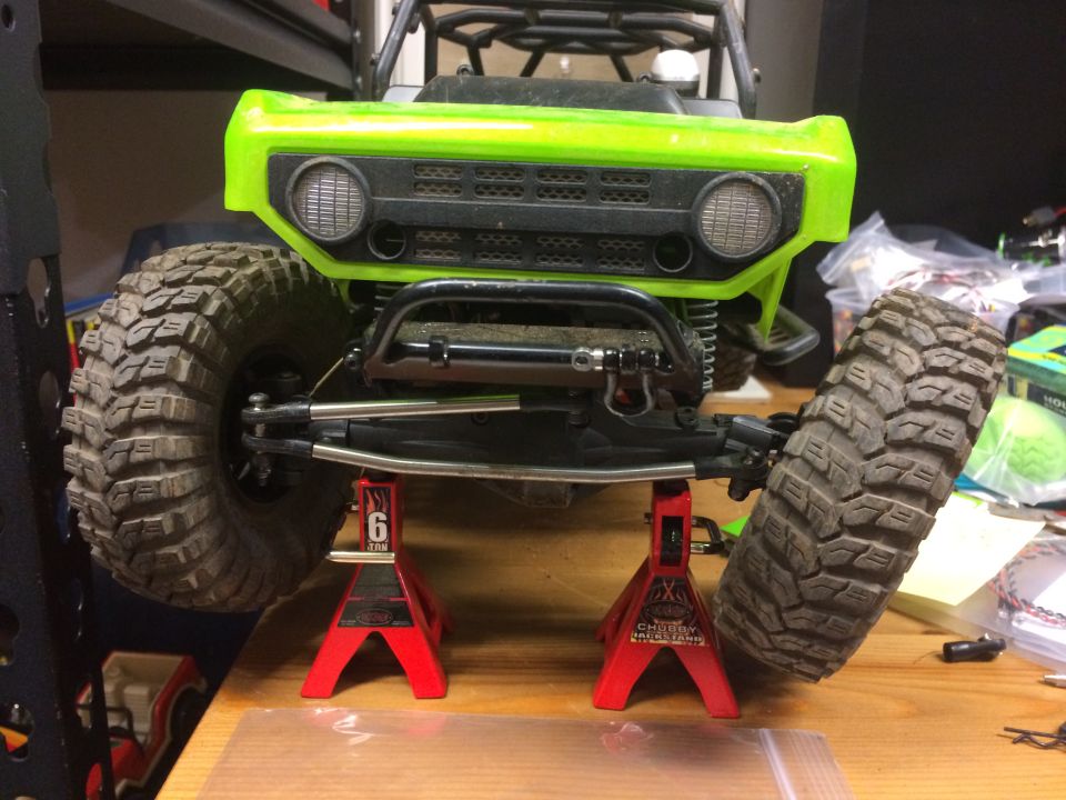 Green RC rock crawler on jack stands, front view. Tires are large and knobby