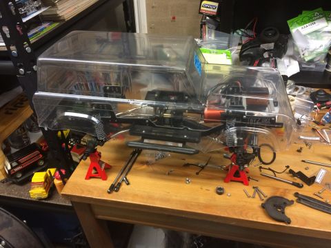 1989 Ford Bronco - RC car chassis with clear body shell, supported by red jack stands on a wooden workbench.