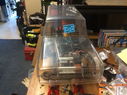 1989 Ford Bronco - A clear, unpainted RC car body is mounted on jack stands, revealing its internal structure and electronics.