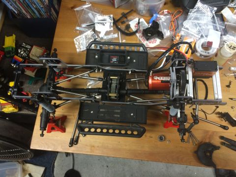 1989 Ford Bronco - The chassis of a remote-controlled car is shown, an orange motor and various suspension parts laid out on a wooden surface.
