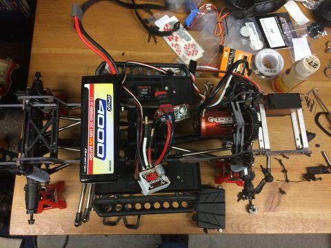 1989 Ford Bronco - RC car chassis assembly with battery, motor, and various electronic components on a wooden surface.