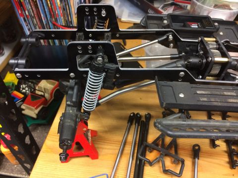 1989 Ford Bronco - Close-up of an unassembled RC car chassis with suspension components and drivetrain parts laid out.