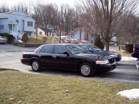 2001 Ford Crown Victoria - A black 2001 Ford Crown Victoria is parked in a driveway with a blue car behind it.