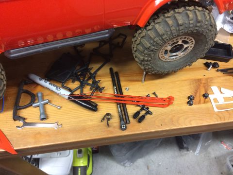 1989 Ford Bronco - A red vehicle's side and tire are visible, surrounded by tools and unassembled parts on a workbench.