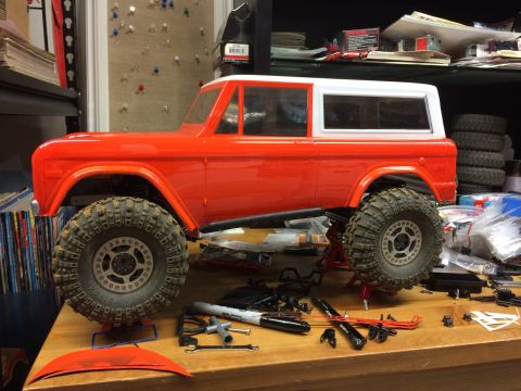 1989 Ford Bronco - This is a side view of a red and white RC car body, possibly a Ford Bronco, sitting on a workbench surrounded by tools and parts.