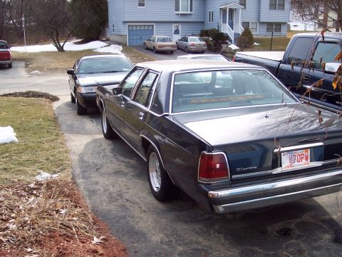 2001 Ford Crown Victoria - A dark sedan parked in a driveway next to other vehicles and a house.