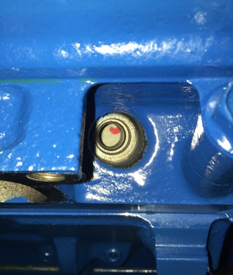 1978 Ford Bronco - A close-up view of a blue engine block shows a small, circular sight glass with a red indicator visible inside. The surrounding metal casin…