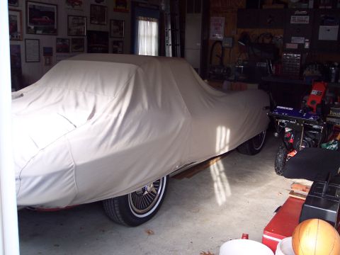2001 Ford Crown Victoria - A vehicle covered by a tan car cover is parked inside a garage, with a snowblower and other items nearby.