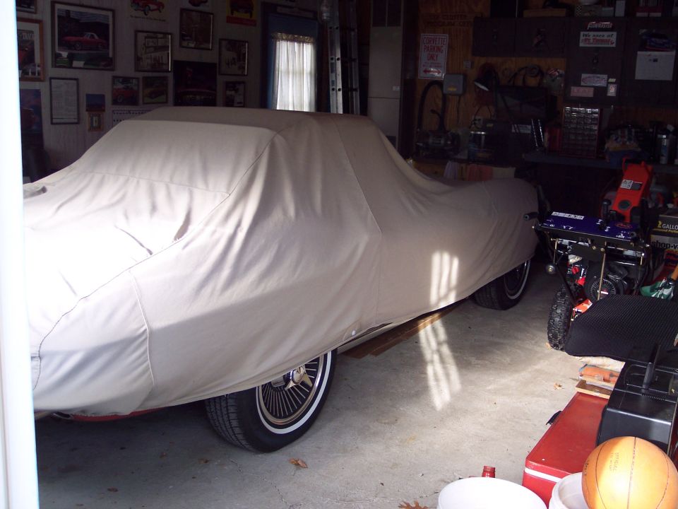 Car covered by tan cover, side view, wire wheels visible