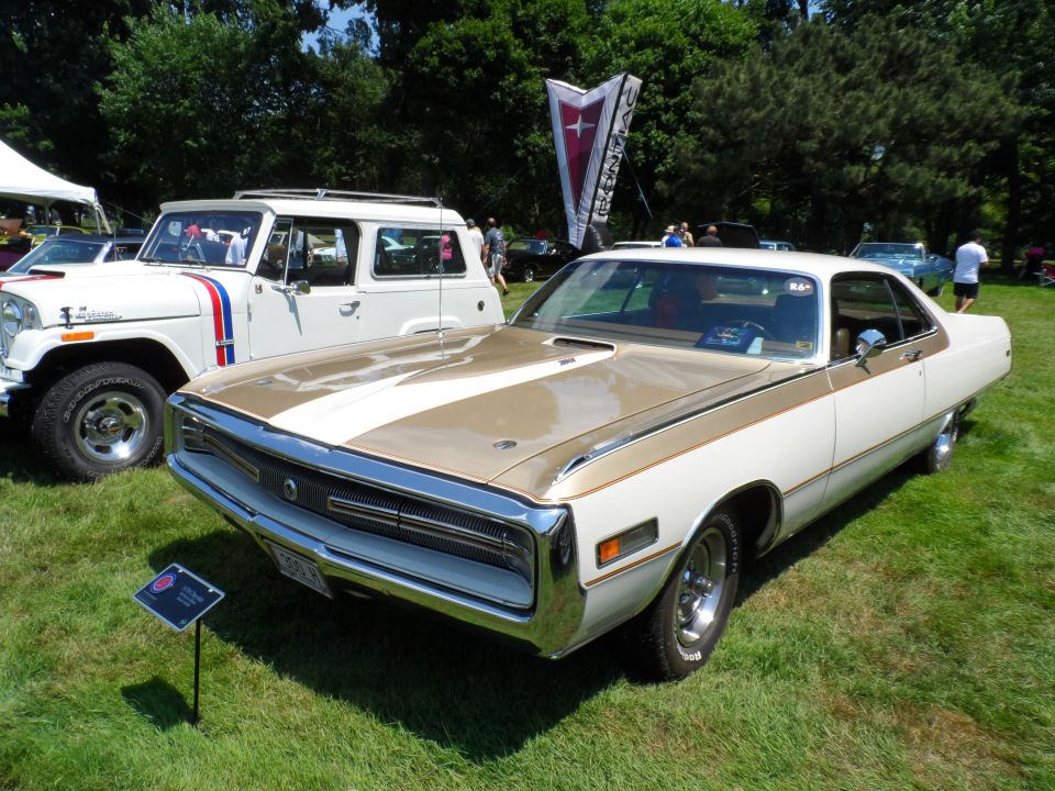 White and gold coupe and white Jeep-like vehicle parked on grass