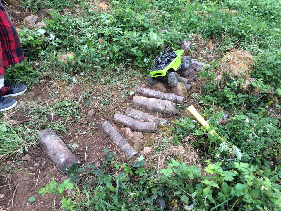 Green RC rock crawler on a log obstacle course.