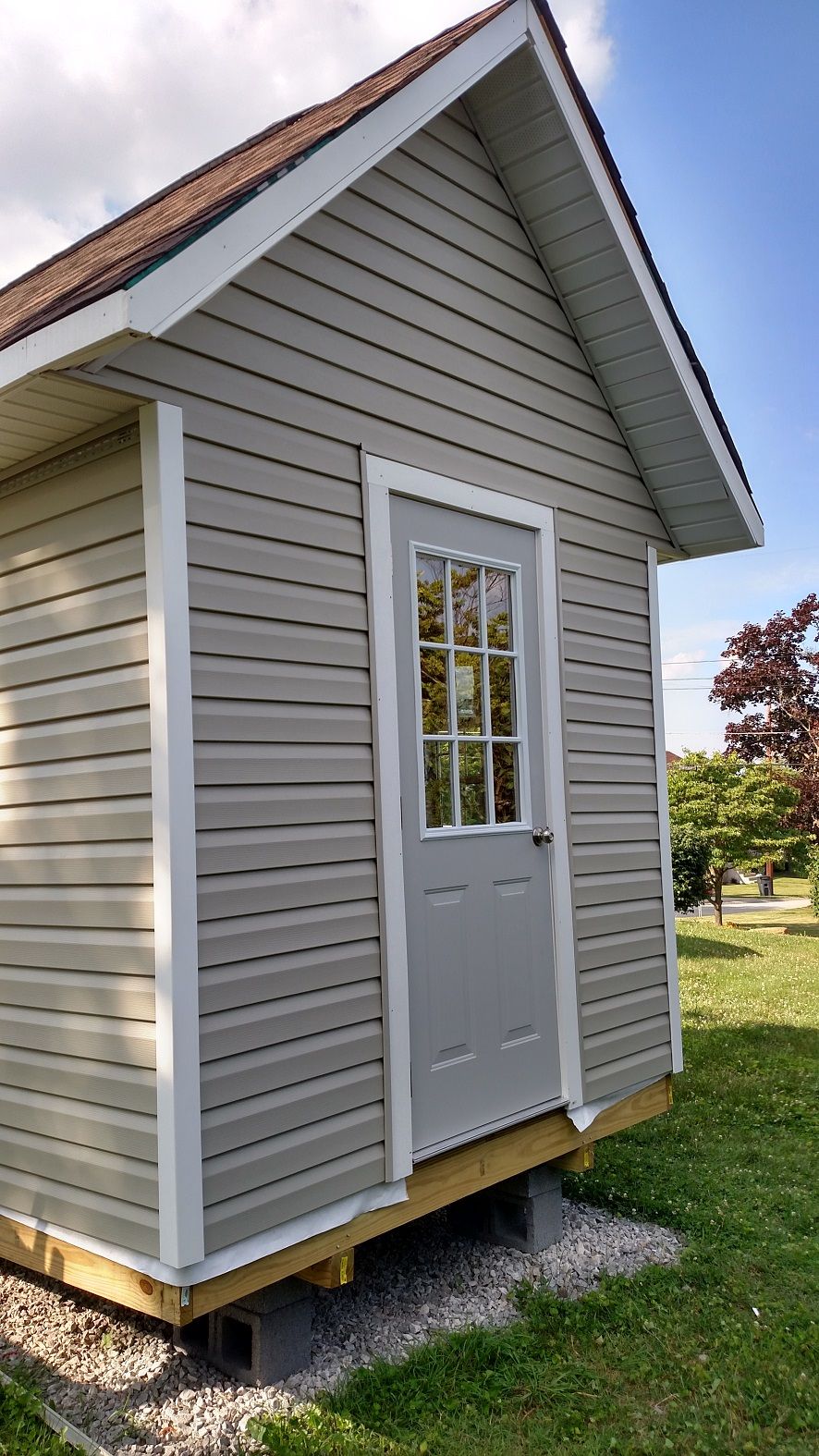 Gray shed with a white-trimmed door and window, set on concrete blocks