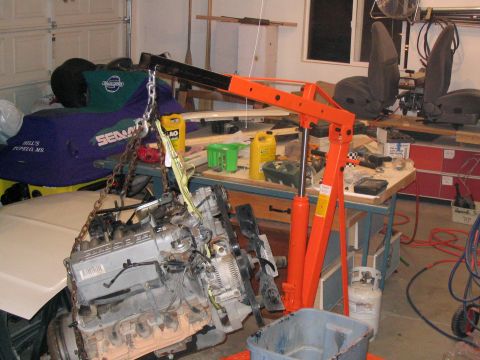 1996 Ford Bronco - Engine hoist lifting an engine in a garage setting with various tools and parts around.