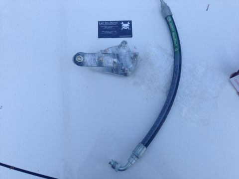 1979 Ford Bronco - A power steering hose and a metal bracket assembly are laid out on a white surface.