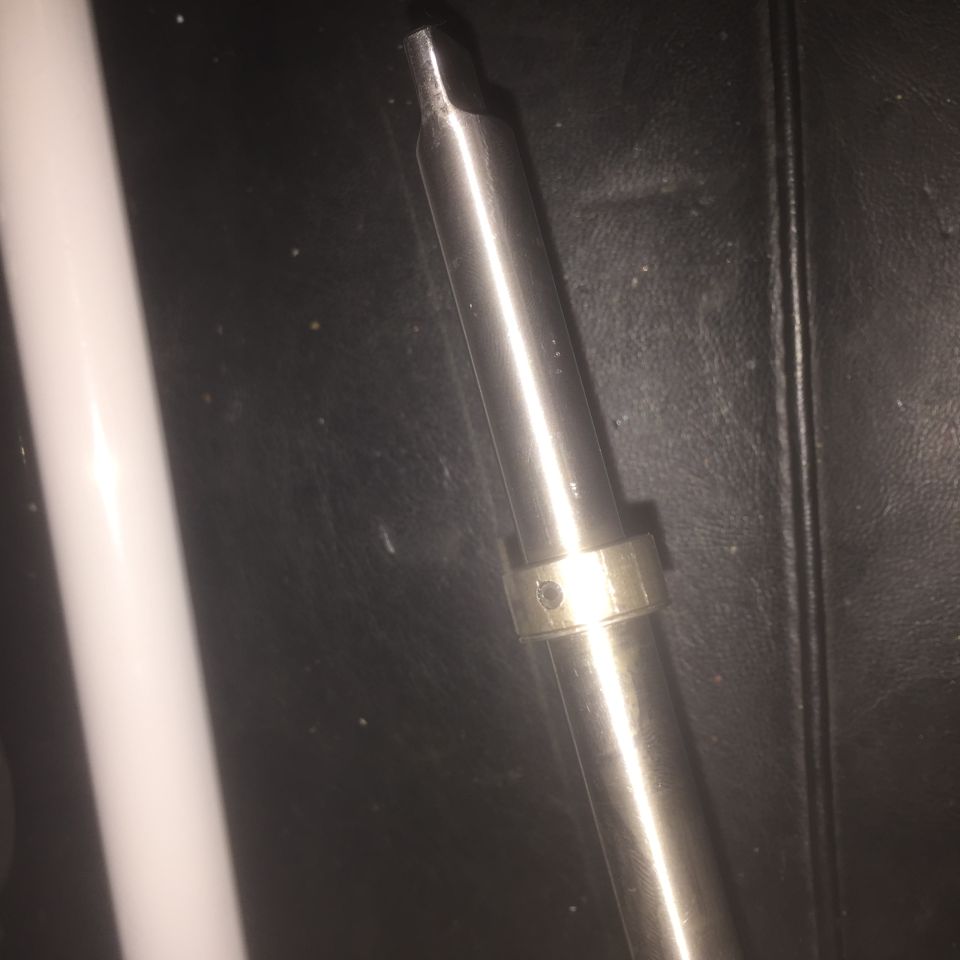 Close-up of a metal rod with a ring and a hole, on a dark surface. Supermotors.net logo visible
