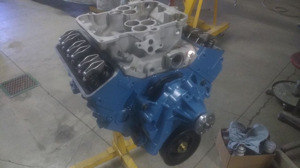 Blue V8 engine on a yellow stand, showing valve covers and intake manifold