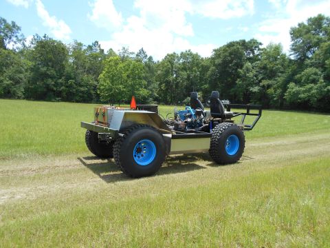 1992 Ford Bronco - Custom off-road vehicle with exposed engine and blue wheels sits in a grassy field under a cloudy sky.