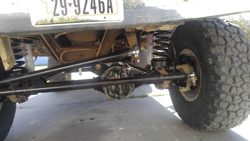 Close-up of off-road suspension with large tires, aftermarket shocks, and a camouflage-covered differential